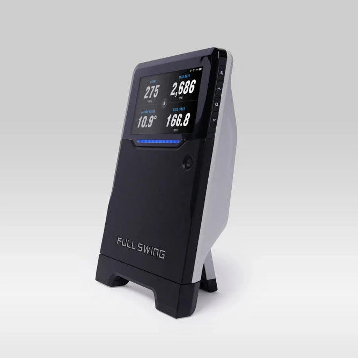 Angled view of the Full Swing launch monitor displaying carry distance, spin rate, launch angle, and ball speed data.