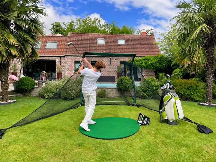 Golfer practising with the Practice Net Pro and side barriers in a garden; round hitting mat and golf bag sold separately