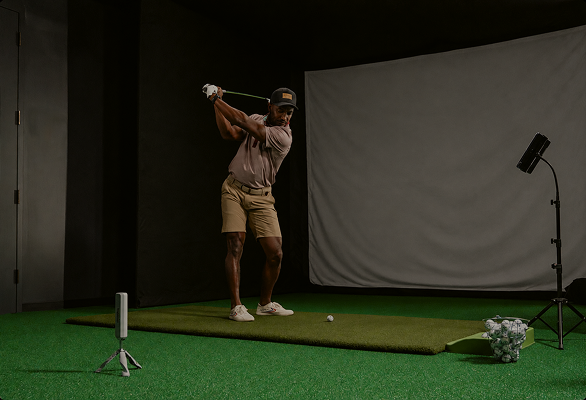 Golfer beim Indoor-Training mit Rapsodo MLM2XPRO neben Abschlagmatte und Impact Screen