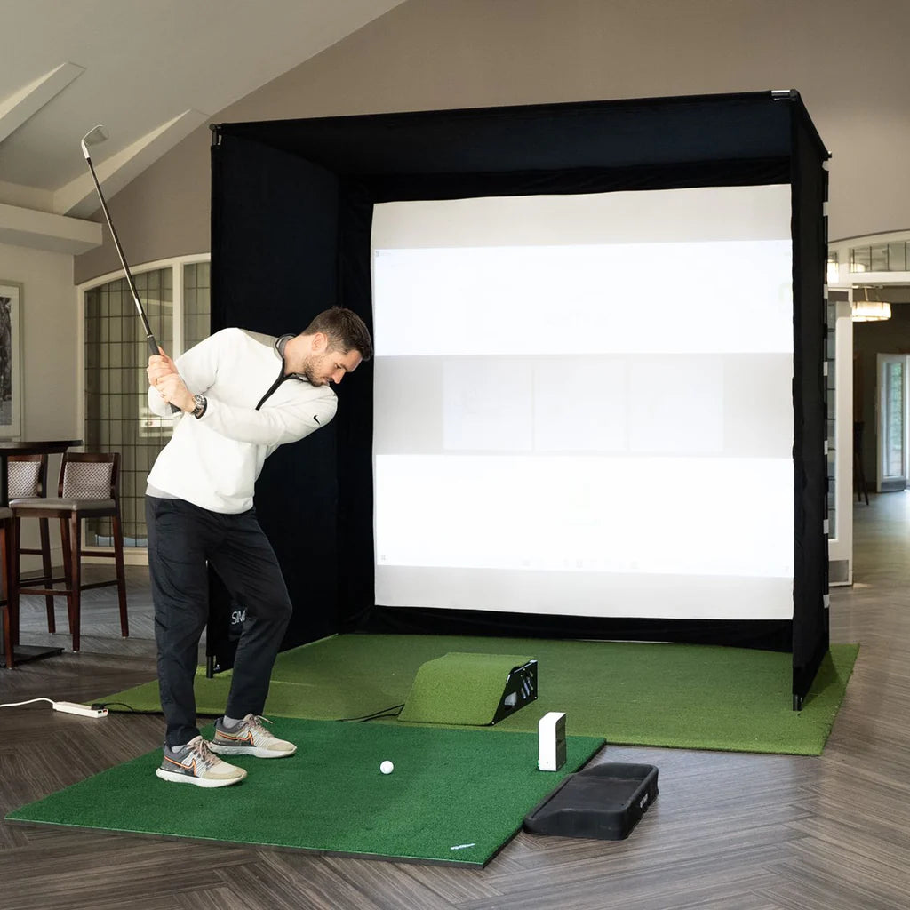 Golfer practicing a swing inside the GolfBays SimBox golf simulator enclosure with impact screen – available at Golf and Greens