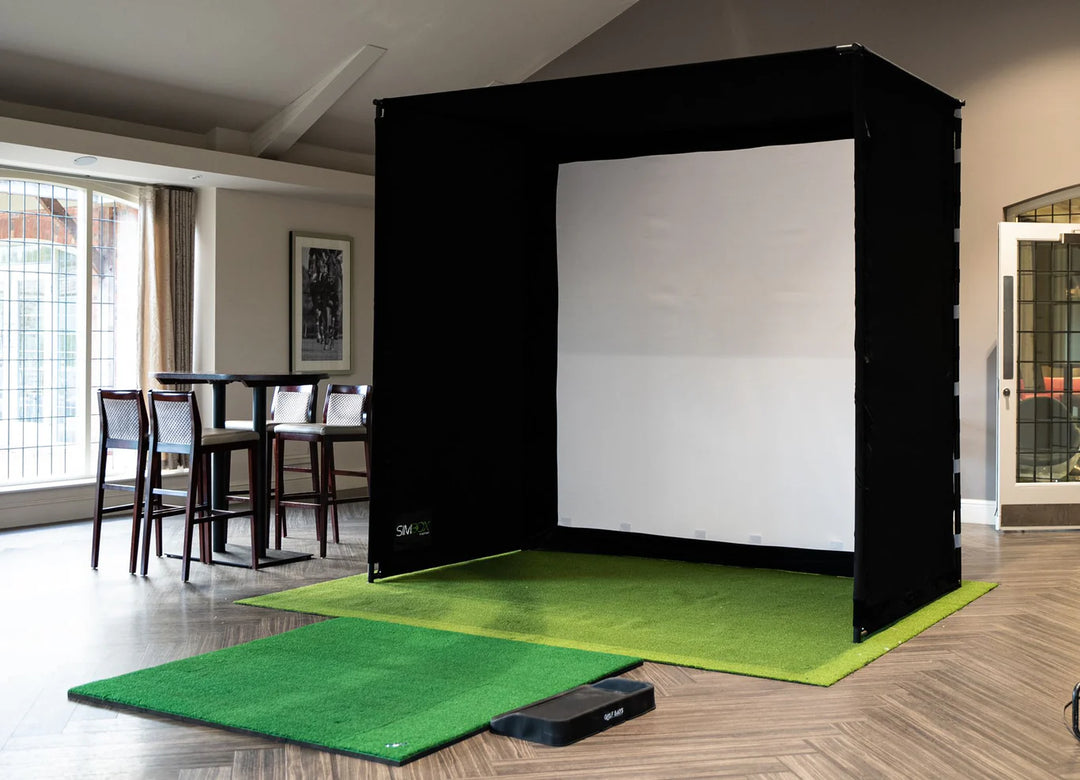 GolfBays SimBox golf simulator enclosure setup in a home room with impact screen and turf mat – available at Golf and Greens