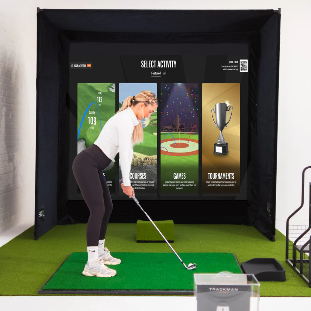Golfer using the GolfBays SimBox golf simulator enclosure with impact screen and putting mat – available at Golf and Greens