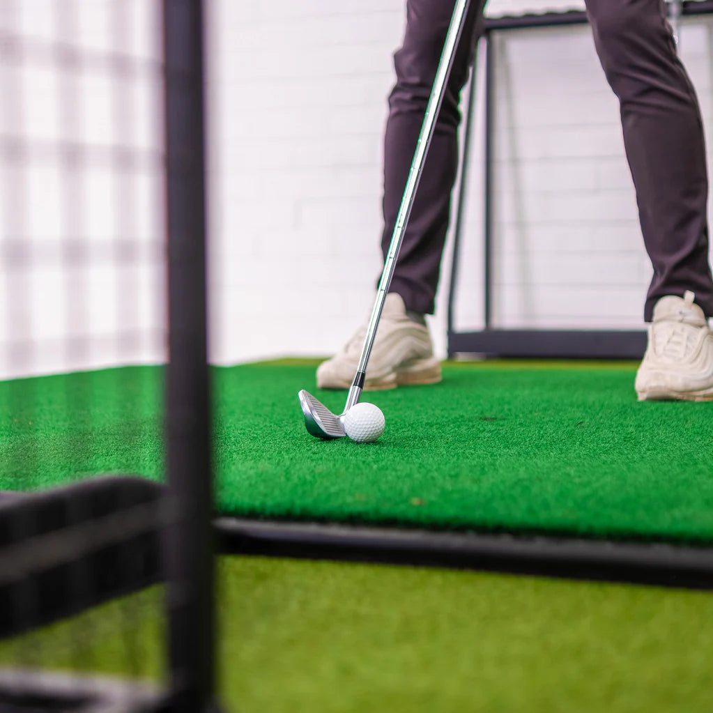 Close-up of golfer hitting a ball inside the GolfBays SimBox golf simulator – available at Golf and Greens